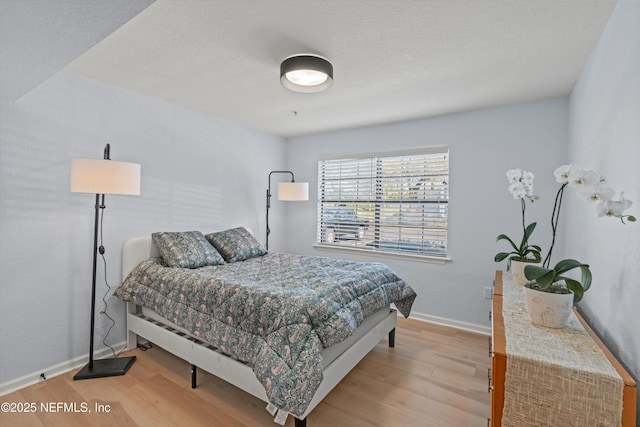 bedroom with a textured ceiling, baseboards, and wood finished floors