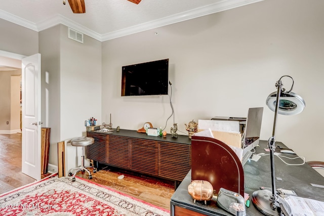 interior space with a ceiling fan, baseboards, wood finished floors, visible vents, and ornamental molding