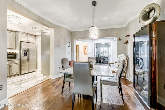 dining room featuring light wood-type flooring, visible vents, baseboards, and crown molding