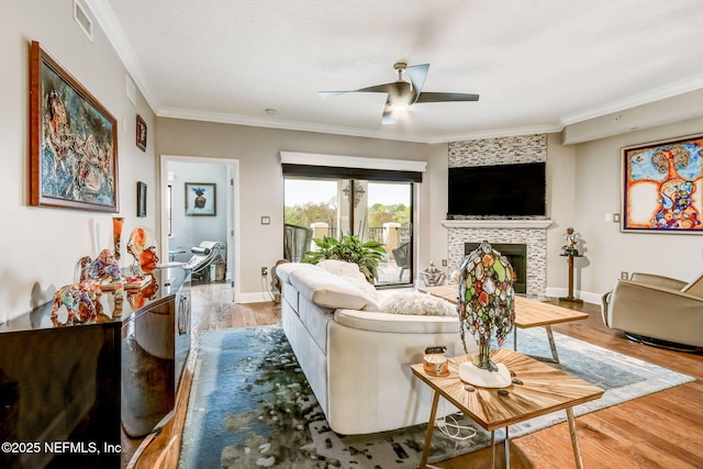 living room featuring ceiling fan, wood finished floors, a tile fireplace, and ornamental molding