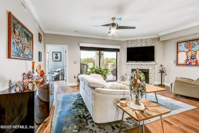 living area featuring visible vents, a ceiling fan, wood finished floors, a fireplace, and crown molding