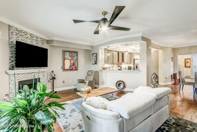 living area featuring baseboards, wood finished floors, a ceiling fan, and crown molding