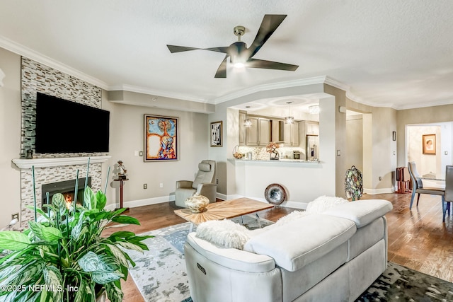 living area featuring wood finished floors, baseboards, a fireplace, ornamental molding, and ceiling fan