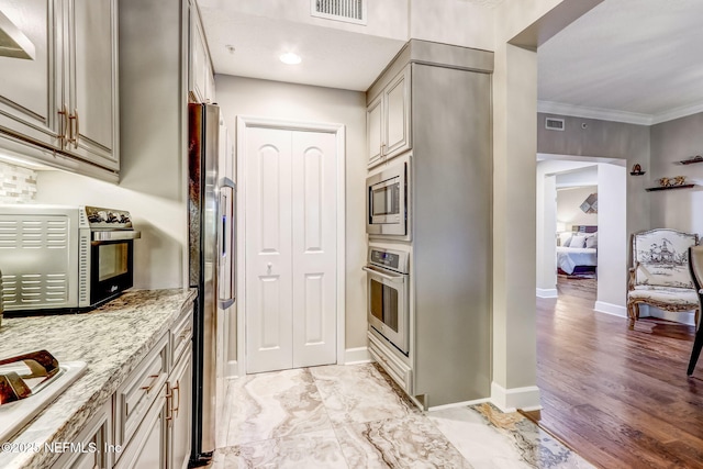 kitchen with light stone countertops, baseboards, visible vents, ornamental molding, and stainless steel appliances