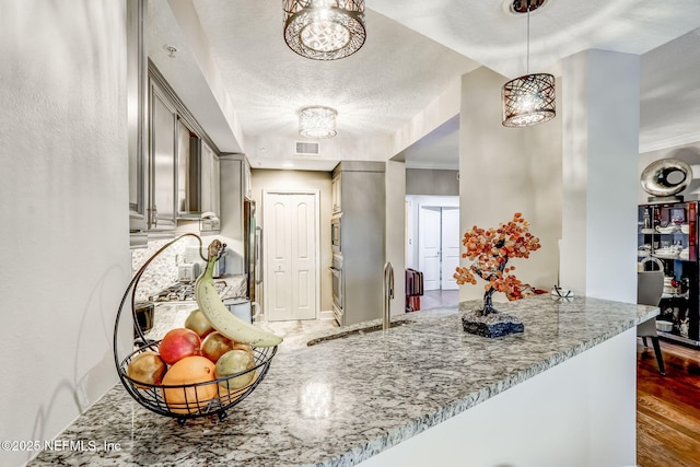 kitchen with gray cabinetry, a sink, wood finished floors, stainless steel appliances, and light stone countertops