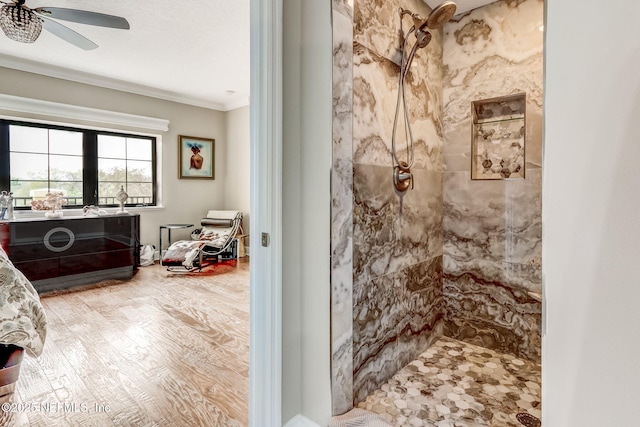 full bath featuring wood finished floors, tiled shower, ornamental molding, and a ceiling fan