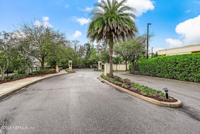 view of street featuring curbs, a gate, a gated entry, street lights, and sidewalks