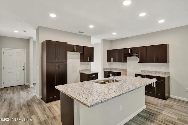 kitchen with light wood finished floors, visible vents, dark brown cabinets, a sink, and a kitchen island with sink