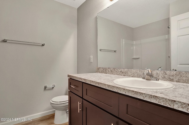 bathroom with vanity, wood finished floors, baseboards, walk in shower, and toilet