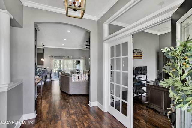 interior space with crown molding, wood finished floors, arched walkways, and baseboards