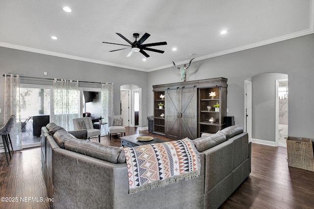 living room featuring baseboards, arched walkways, ornamental molding, ceiling fan, and dark wood-type flooring