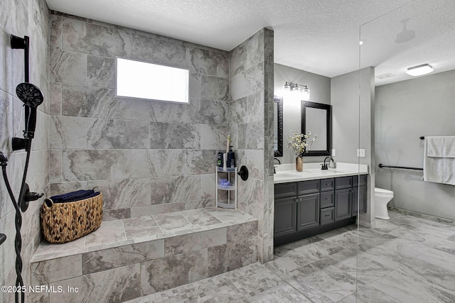 full bath featuring walk in shower, toilet, double vanity, a textured ceiling, and a sink