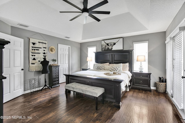 bedroom with visible vents, a raised ceiling, and dark wood-type flooring