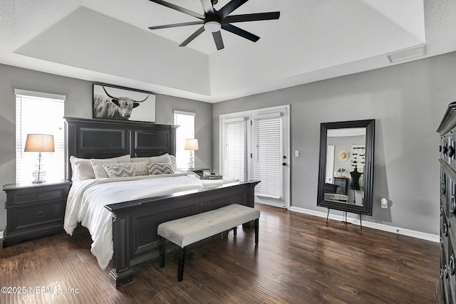 bedroom featuring a ceiling fan, dark wood-style floors, baseboards, visible vents, and a tray ceiling