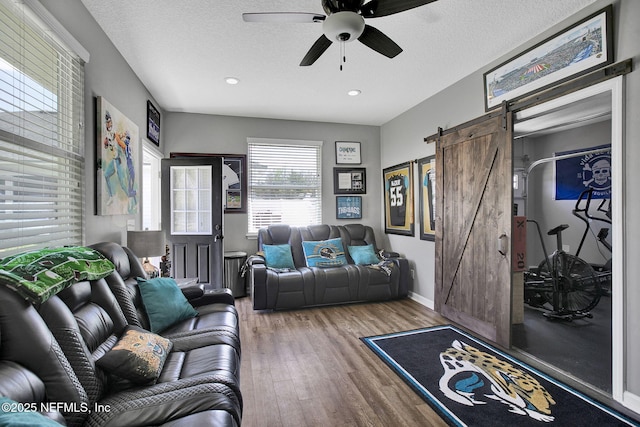 living area featuring a textured ceiling, a ceiling fan, a barn door, and wood finished floors