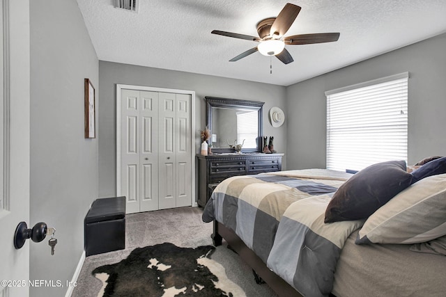 carpeted bedroom featuring a ceiling fan, visible vents, a closet, and a textured ceiling