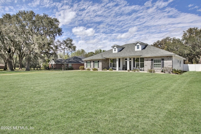 rear view of property featuring a lawn, roof with shingles, brick siding, and fence