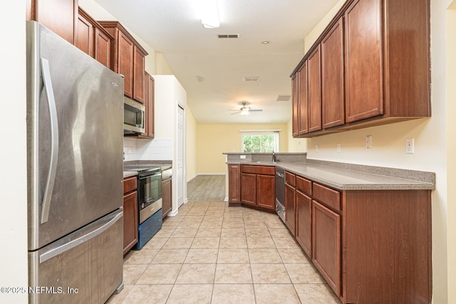 kitchen with a peninsula, light tile patterned flooring, stainless steel appliances, a ceiling fan, and a sink