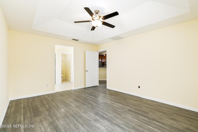 empty room featuring wood finished floors, baseboards, visible vents, ceiling fan, and a raised ceiling