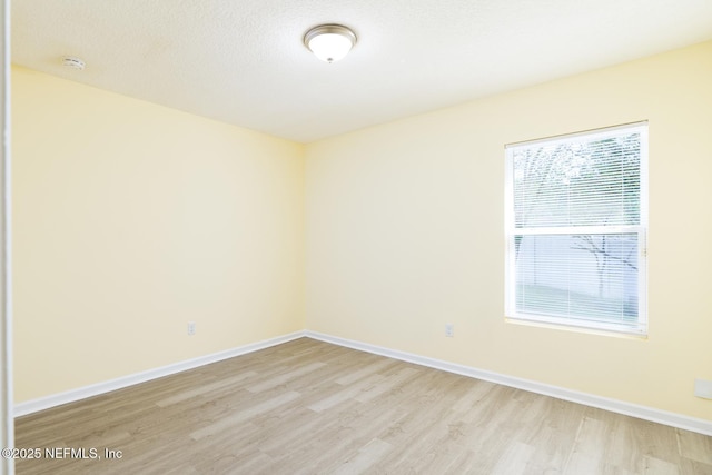 spare room featuring baseboards, light wood finished floors, and a textured ceiling