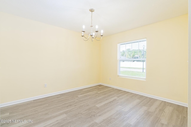 unfurnished room featuring a notable chandelier, baseboards, and light wood-style floors