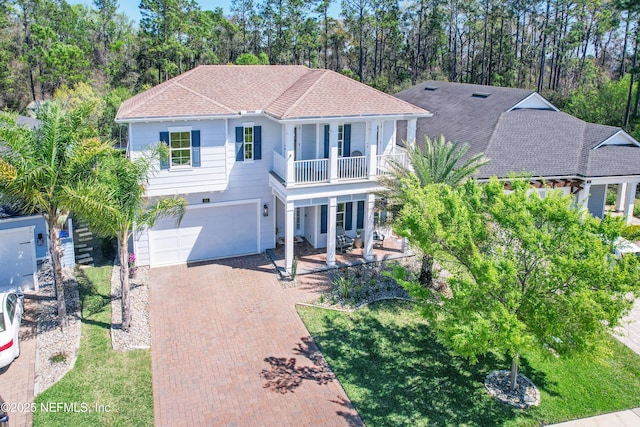 view of front of home with decorative driveway, covered porch, a front yard, an attached garage, and a balcony