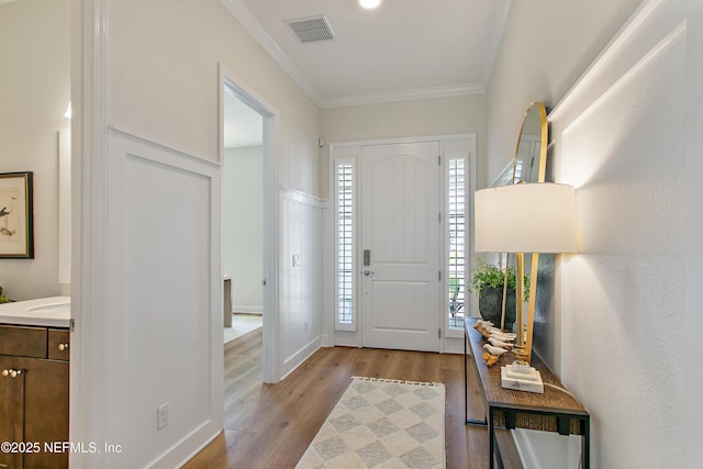 foyer entrance with visible vents, ornamental molding, and light wood finished floors