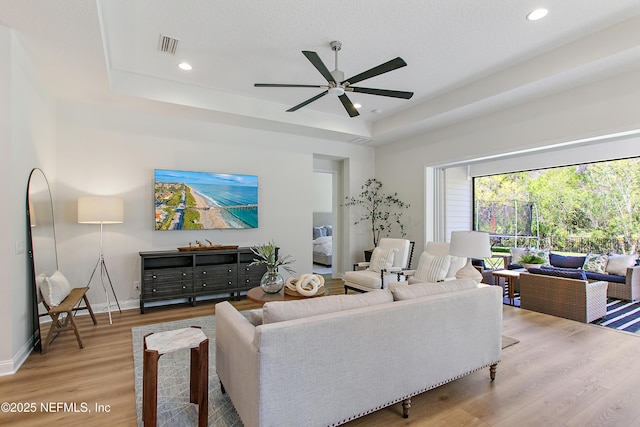 living room with recessed lighting, a tray ceiling, light wood-style floors, and a ceiling fan