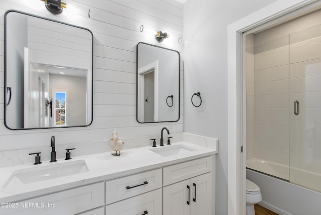 bathroom with double vanity, toilet, bath / shower combo with glass door, and a sink