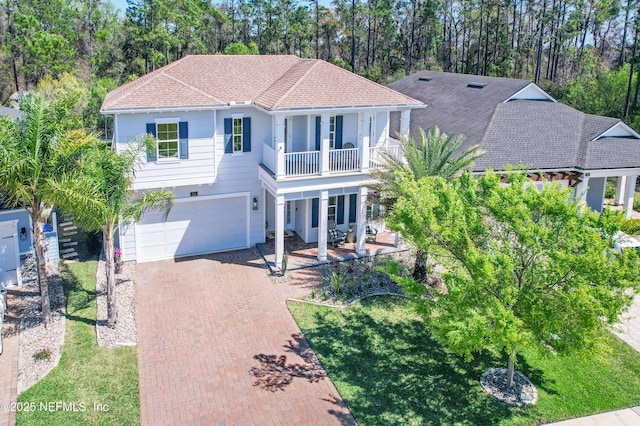 view of front of property featuring a porch, roof with shingles, decorative driveway, a balcony, and an attached garage