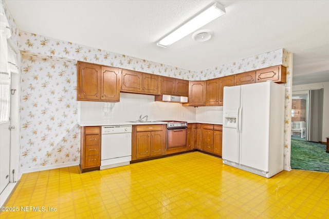 kitchen featuring white appliances, baseboards, wallpapered walls, a sink, and light countertops