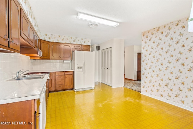 kitchen with brown cabinetry, white refrigerator with ice dispenser, light countertops, and wallpapered walls