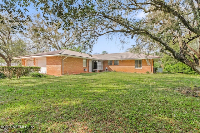 rear view of property with a yard, brick siding, an attached garage, and metal roof