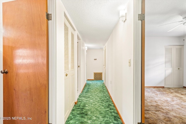 corridor with a textured ceiling, baseboards, and carpet floors