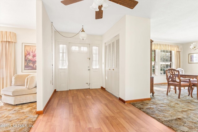 entrance foyer with ceiling fan with notable chandelier, baseboards, and light wood-style floors