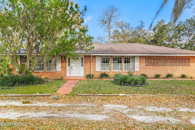 ranch-style home featuring a front lawn, brick siding, and metal roof