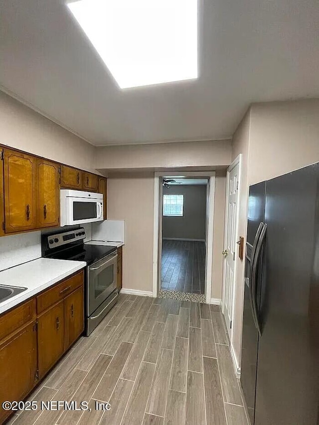 kitchen featuring stainless steel electric range oven, white microwave, wood finish floors, light countertops, and black fridge