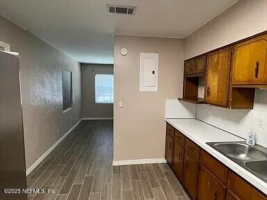 kitchen with baseboards, visible vents, electric panel, a sink, and dark wood-type flooring