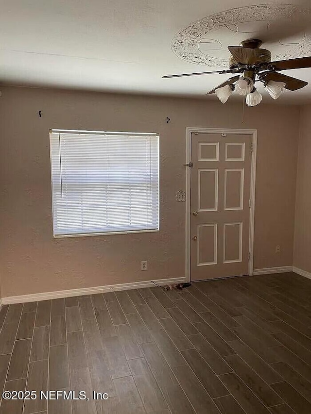 empty room with ceiling fan, dark wood-type flooring, and baseboards