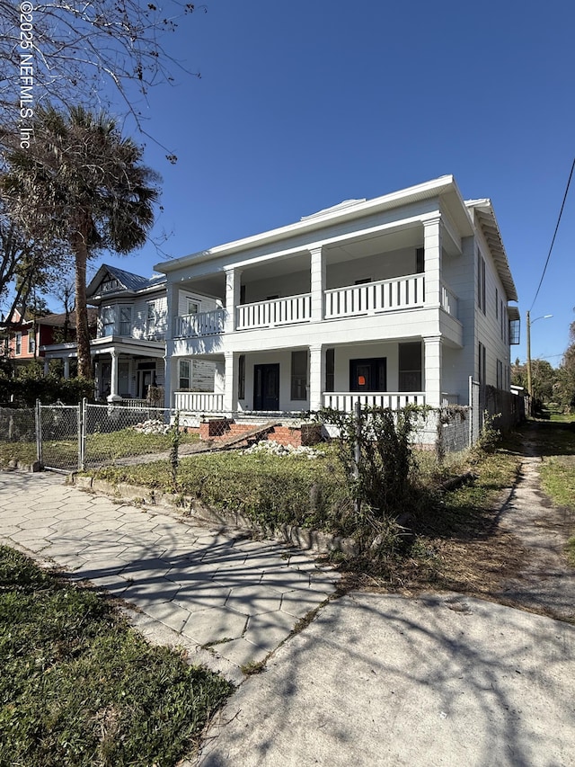 back of house featuring a balcony, a gate, fence, and covered porch