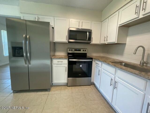 kitchen with dark stone counters, a sink, decorative backsplash, stainless steel appliances, and white cabinetry