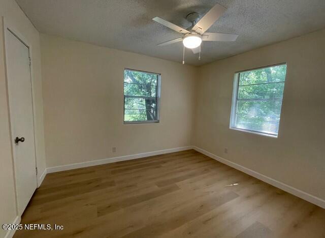 empty room featuring baseboards, a textured ceiling, a healthy amount of sunlight, and wood finished floors