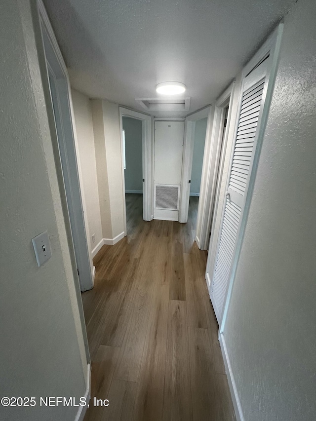 hall with visible vents, baseboards, and wood finished floors