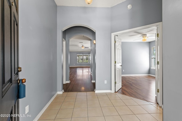 entryway with light tile patterned floors, a ceiling fan, arched walkways, and baseboards