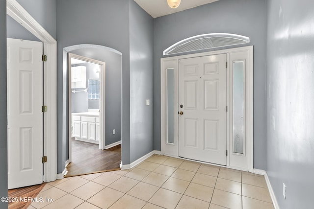 entryway with light tile patterned floors, arched walkways, and baseboards