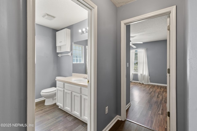 bathroom with visible vents, toilet, a textured ceiling, wood finished floors, and vanity