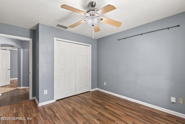 unfurnished bedroom with visible vents, a textured ceiling, wood finished floors, a closet, and arched walkways