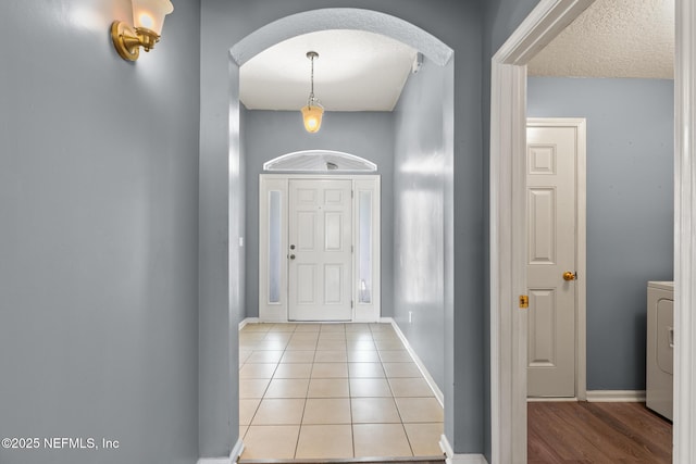 entryway with baseboards, light tile patterned floors, washer / dryer, arched walkways, and a textured ceiling