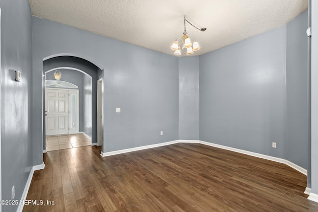 spare room featuring arched walkways, a textured ceiling, an inviting chandelier, and dark wood-style flooring