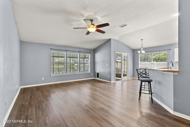 unfurnished living room with dark wood-style floors, visible vents, ceiling fan with notable chandelier, and vaulted ceiling